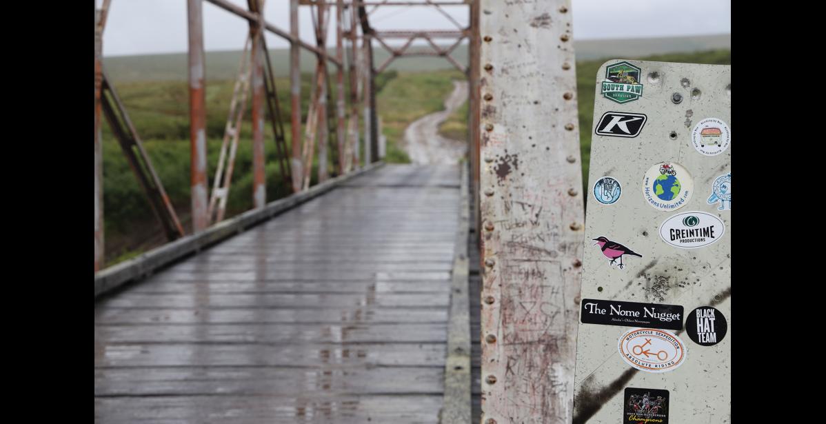 Photo by Colin Warren END OF ROAD STICKERS – A sign with random stickers mark the Kougarok Bridge